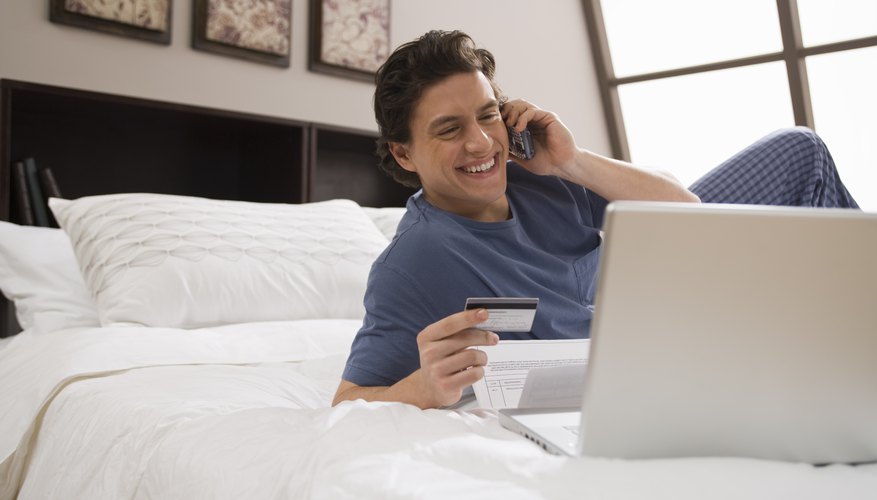 Man holding a credit card in front of a computer while on the phone.