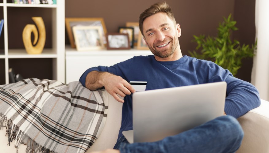 Smiling man with laptop and credit card on sofa