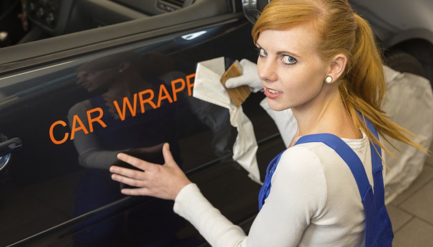 Worker affixes car wrapping foil for advertisement on vehicle