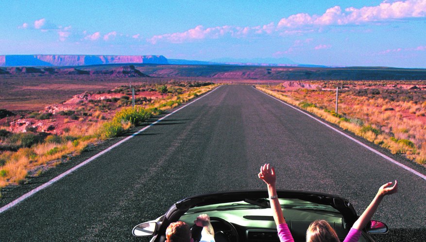 Photo, couple riding in a convertible on a desert highway, woman has her arms in the air, rear view, Color, Low res