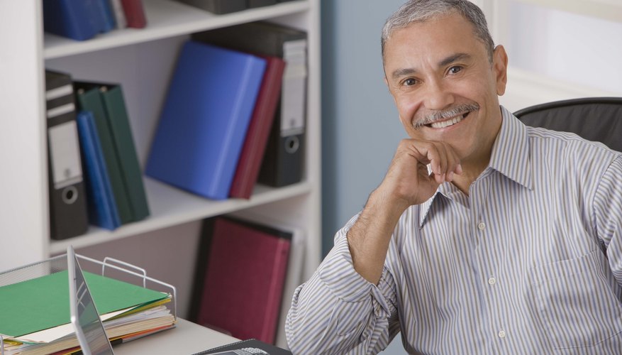 A smiling man is sitting in front of his laptop at his desk.