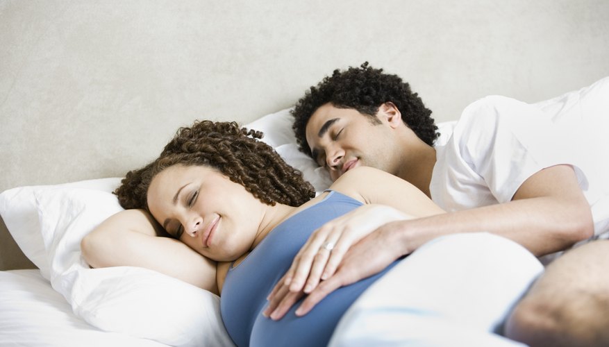 Young pregnant woman sleeping beside her husband in bed. Young pregnant woman sleeping beside her husband in bed.