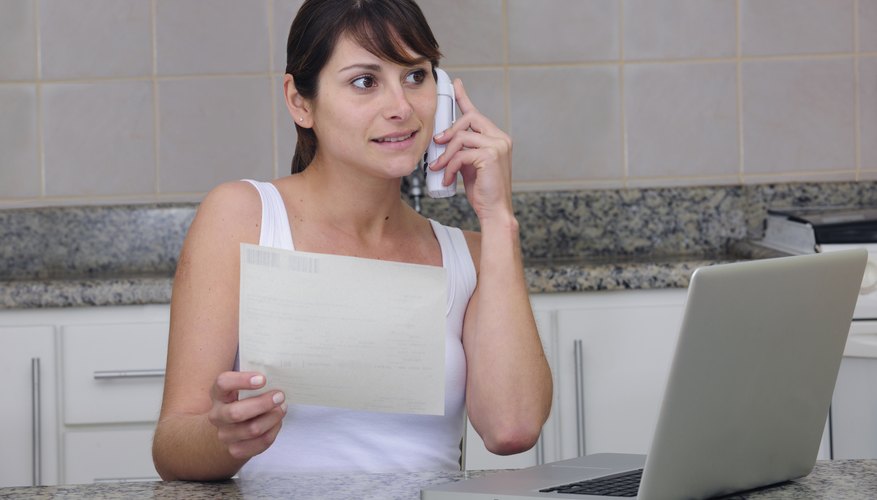 A woman is working on her laptop and talking on the phone.