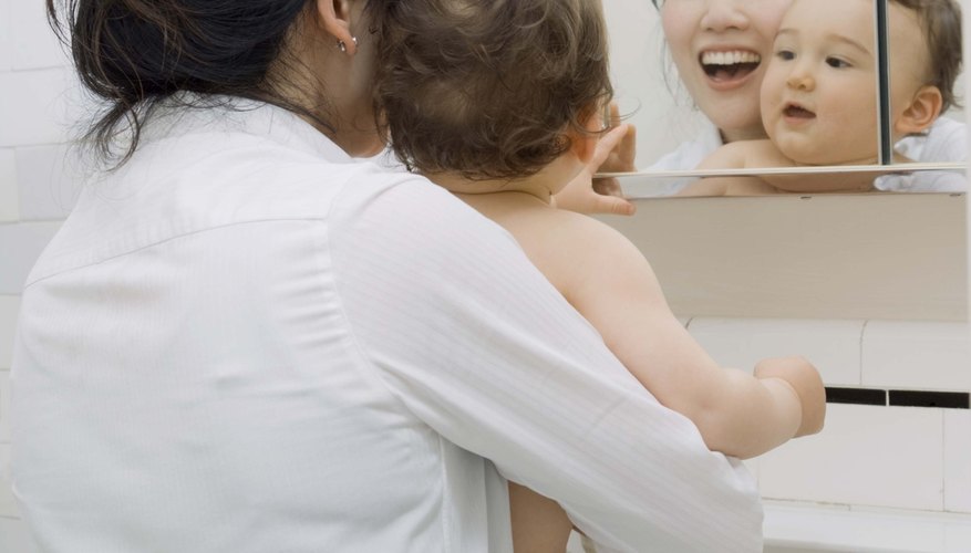 Around 12 months of age, a toddler develops self-awareness and recognizes her reflection in the mirror. Around 12 months of age, a toddler develops self-awareness and recognizes her reflection in the mirror.