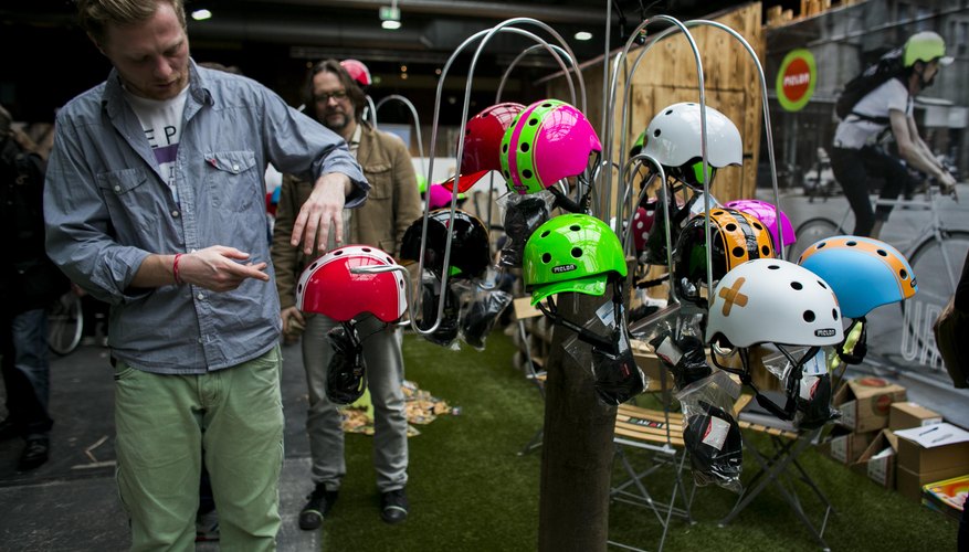 Photo Credit: Carsten Koall/Getty Images News/Getty Images Man standing next to assortment of bicycle helmets