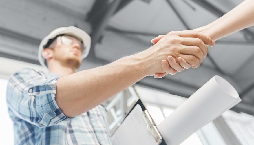 builder with blueprint shaking partner hand