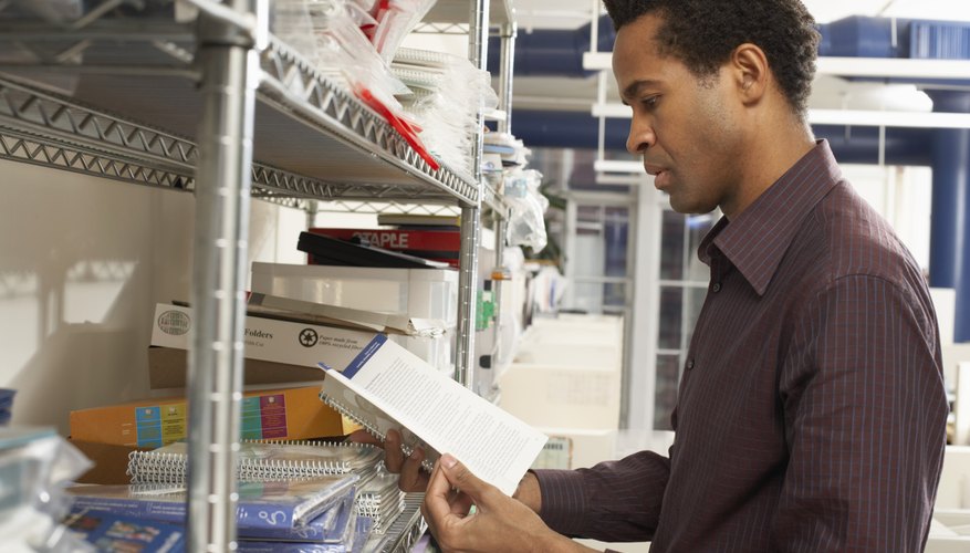 Male office worker looking at exercise book by storage shelves