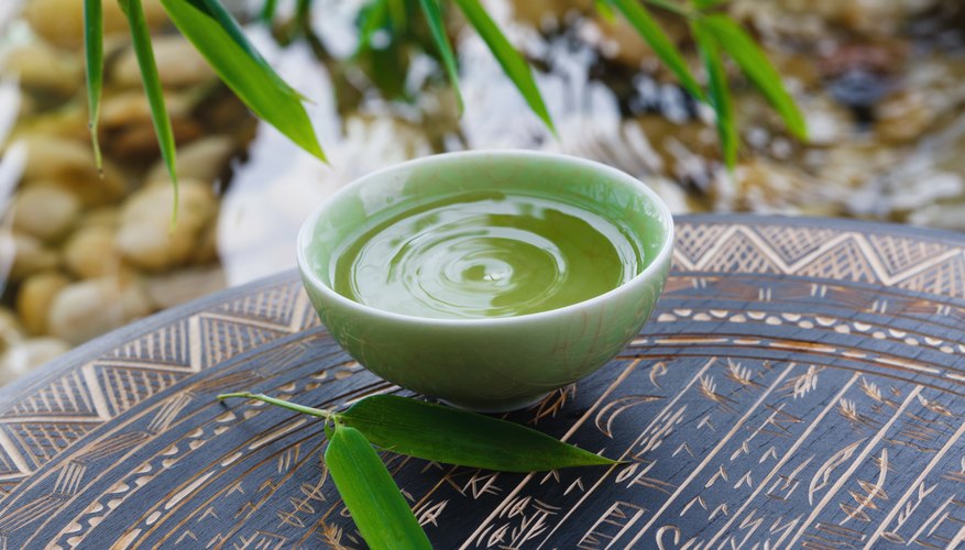 A cup of green tea on a tray near a stream. A cup of green tea on a tray near a stream.