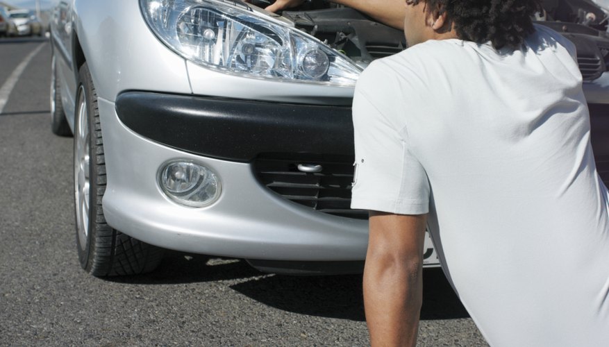 Man sitting on road fixing car with open bonnet, rear view