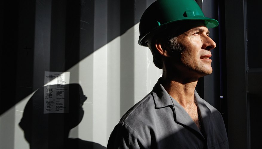 A man with a hard hat on looks out to a worksite as the sun comes in.