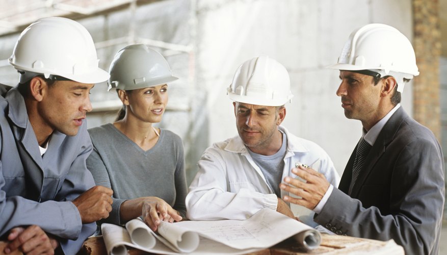 Men and women in hardhats looking at blueprints on construction site