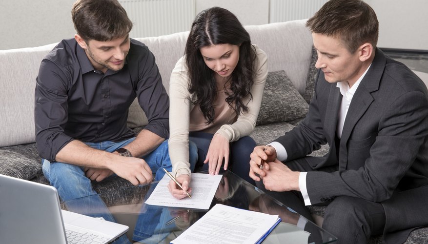 A couple signing documents, sitting next to a real estate agent