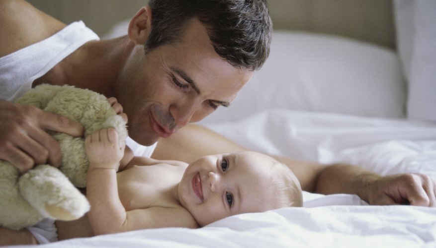 Father holding stuffed animal up to infant on bed. Father holding stuffed animal up to infant on bed.