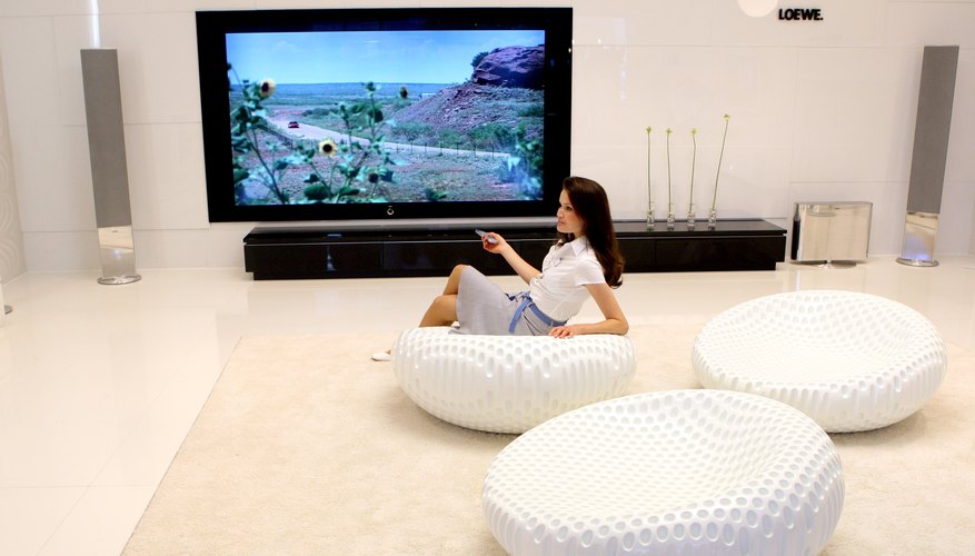 Photo Credit: Marcel Mettelsiefen/Getty Images News/Getty Images Woman with large LCD television and modern furnishings