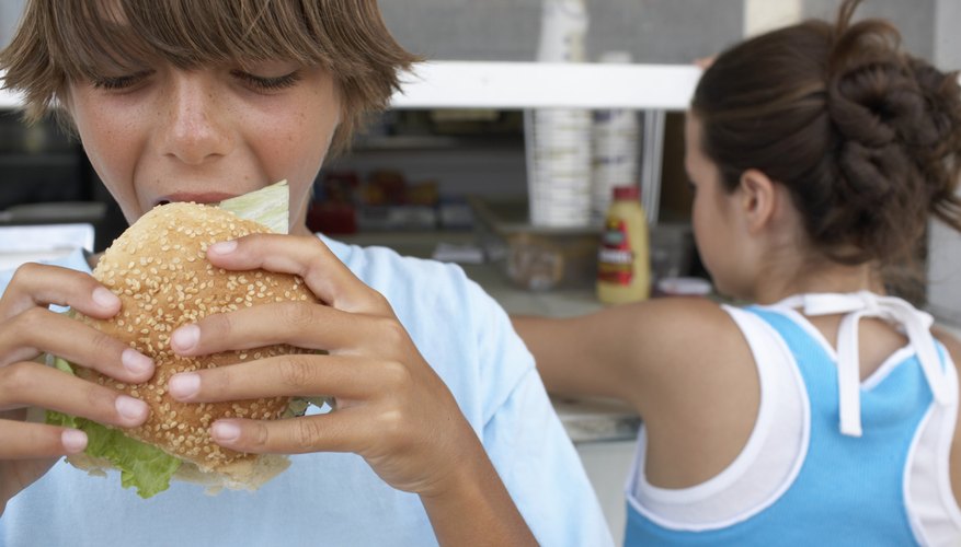 A boy eats a hamburger in front of a take-out stand. A boy eats a hamburger in front of a take-out stand.