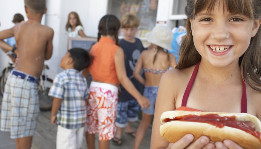 Girl (8-10) holding hotdog, smiling, portrait, children in background