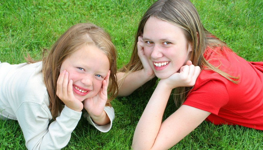 A teenage girl and younger girl lay on a patch of grass. A teenage girl and younger girl lay on a patch of grass.