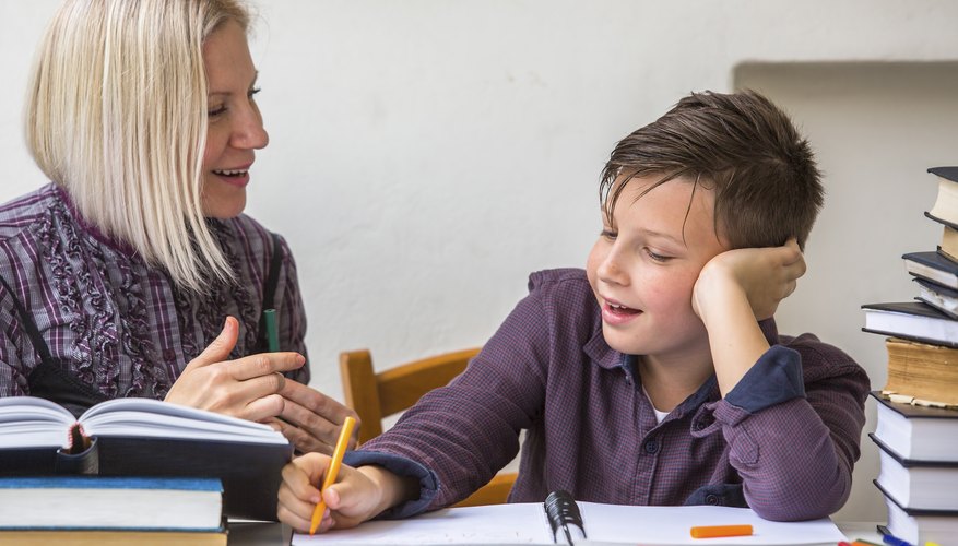 A tutor helping a boy surrounded by his books complete his homework.