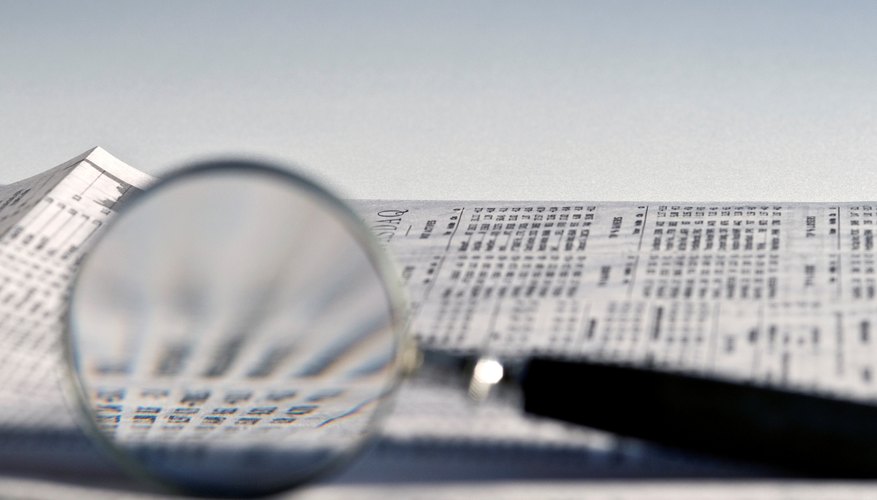 Magnifying glass highlighting investment stock quotes in business section of newspaper.