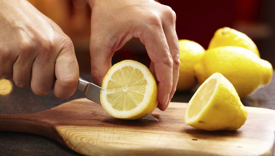 Photo Credit: Paul Johnson/iStock/Getty Images Hand slicing lemons on cutting board.