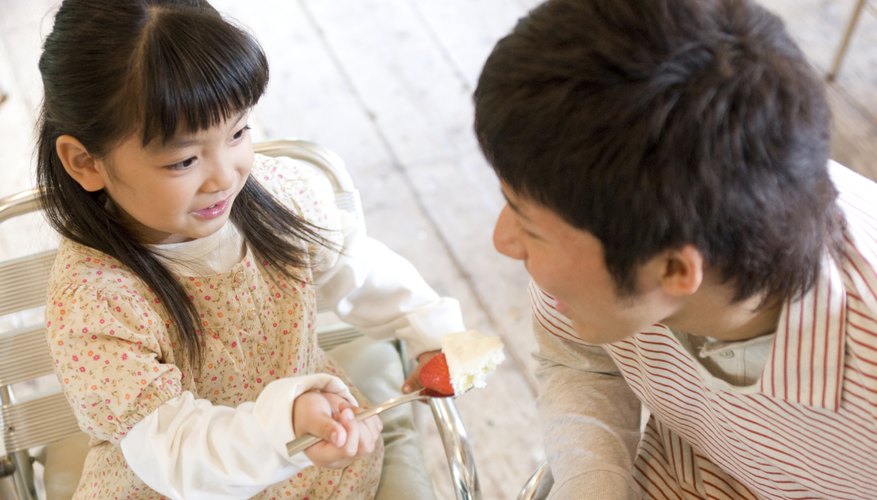 Child sharing piece of cake with her father Child sharing piece of cake with her father