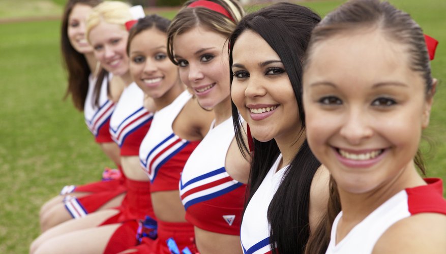 Photo Credit: Digital Vision./Photodisc/Getty Images Smiling cheerleaders sitting on bench.