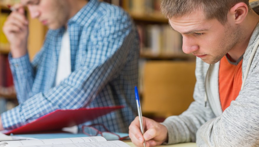 Student working on homework without calculator in library. Student working on homework without calculator in library.