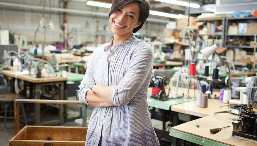 Photo Credit: Image Source/Digital Vision/Getty Images Woman standing in small clothing line warehouse