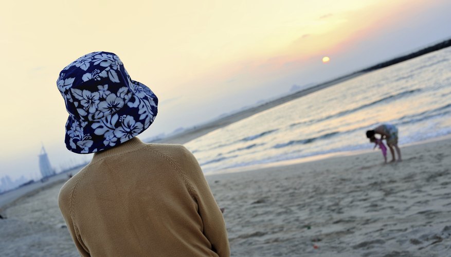 A woman watching her young child and spouse on the beach.