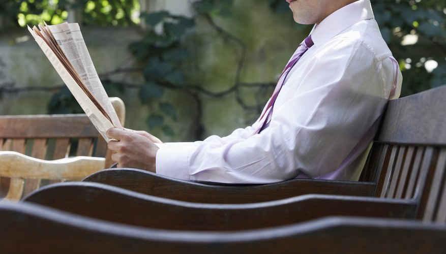 Businessman sitting on bench in park garden reading paper, mid section