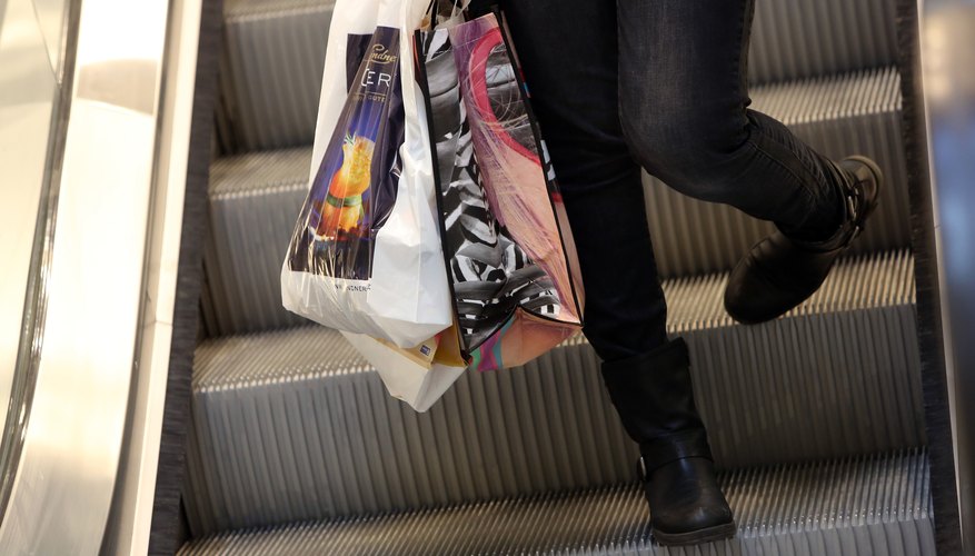 A woman carrying department store shopping bags down the escalator in a mall.