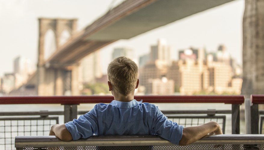 A young boy sits on a bench overlooking a bridge in New York City. A young boy sits on a bench overlooking a bridge in New York City.
