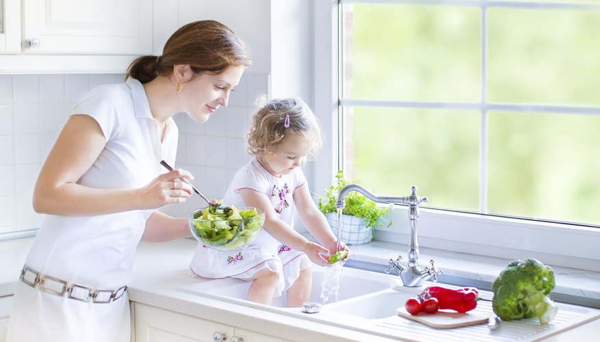 Girl and mother washing vegetables in kitchen sink Girl and mother washing vegetables in kitchen sink