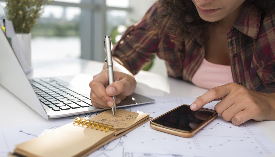 Woman writing down phone number beside laptop