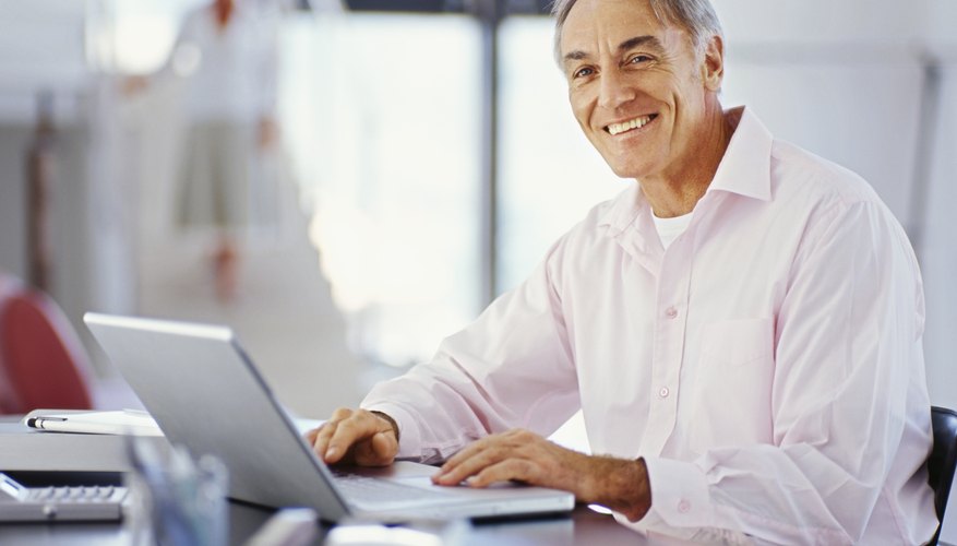 Elderly man researching on laptop in home office.