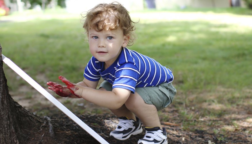 A two-year-old boy makes a finger painting on a canvas in the backyard. A two-year-old boy makes a finger painting on a canvas in the backyard.