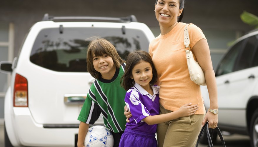 Two children dressed in soccer uniforms hug their mom in a parking lot. Two children dressed in soccer uniforms hug their mom in a parking lot.