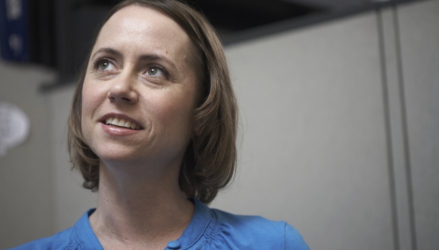 Woman in office cubicle, looking up and smiling