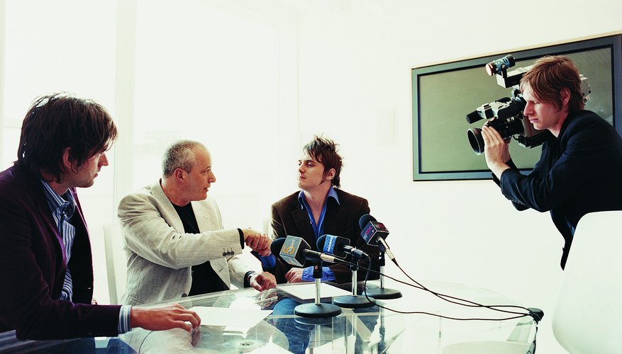 Pop Musician Shaking Hands With a Businessman at a News Conference With Microphones and a TV Cameraman