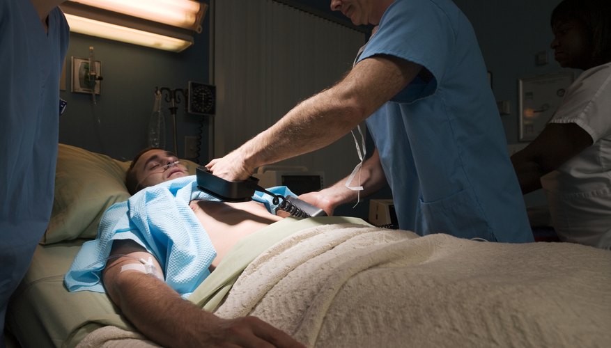 Doctors defibrillating patient in hospital bed