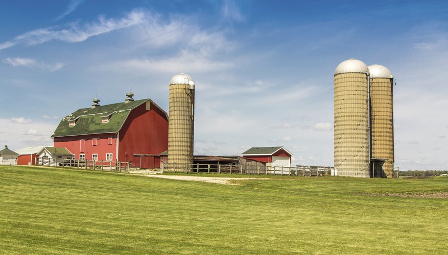 Photo Credit: Marcin Leszczuk/iStock/Getty Images A barn and silos on farmland.