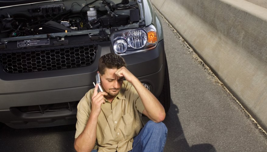 Man sitting next to broken down car on highway