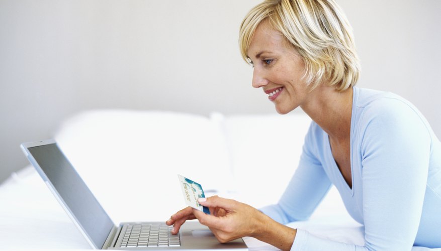 Woman holding up a credit card and working on a laptop.