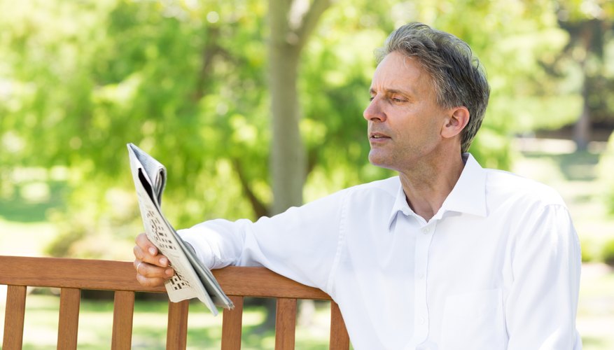 Photo Credit: Wavebreakmedia Ltd/Wavebreak Media/Getty Images Man reading a newspaper on a park bench