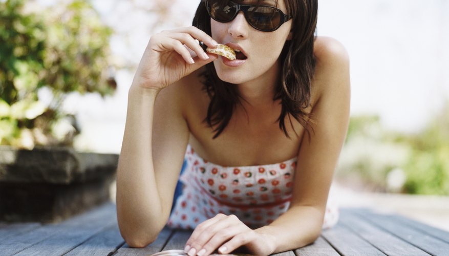 Woman Lying on Decking Reading a Magazine and Eating an Orange