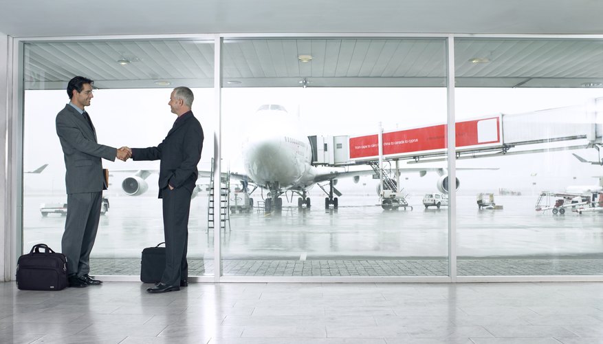 Two businessmen shaking hands in airport, smiling, side view