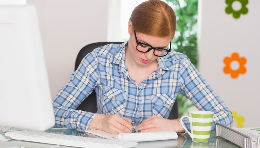 Redhead writing on notepad at her desk