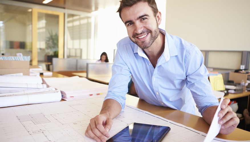 Male Architect With Digital Tablet Studying Plans In Office