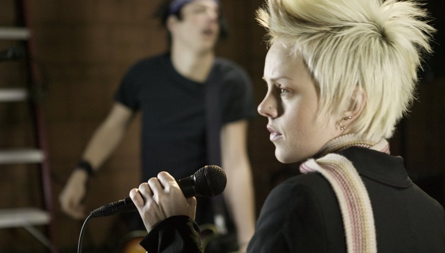 Young woman singing at microphone, man playing guitar, in studio