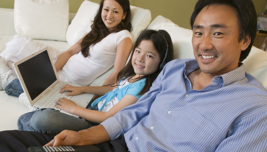 Photo Credit: Mike Watson Images/moodboard/Getty Images A family watches television and use a laptop in the living room together